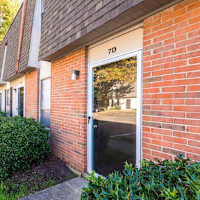 A building with the number 7D on it has a door open and a bush in front.