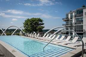 A Beautiful pool with chairs and a building in the background. at Dock 79, Washington, DC