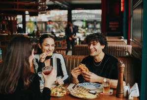 three people eating pizza at a table in a restaurant