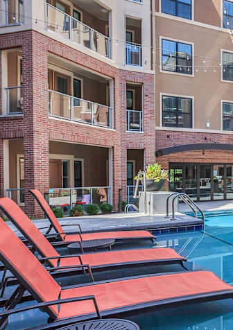 A pool with red sun loungers in front of apartment buildings.
