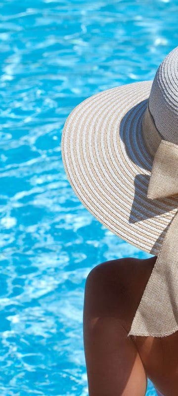 a woman wearing a hat and looking at a swimming pool
