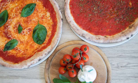 two pizzas on a table with tomatoes and cheese and basil at The Villages Apartment of Bayan Grove in Boynton Beach, FL