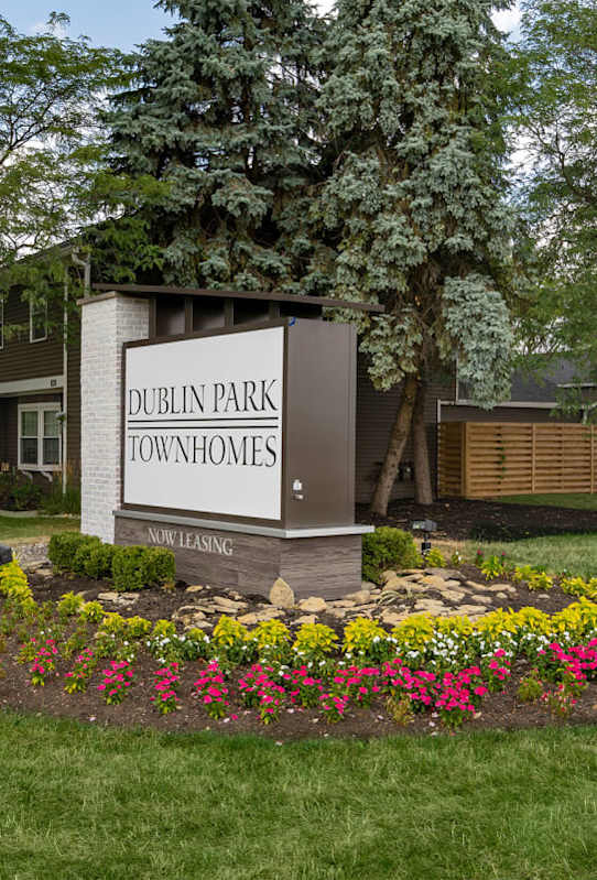 A sign for Dublin Park Townhomes is surrounded by flowers and greenery.