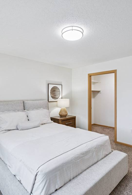 A bedroom with a large bed and two nightstand with lamps, and attached walk-in closet