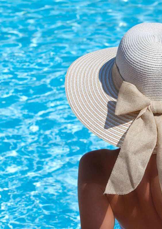 a woman wearing a hat and looking at a swimming pool