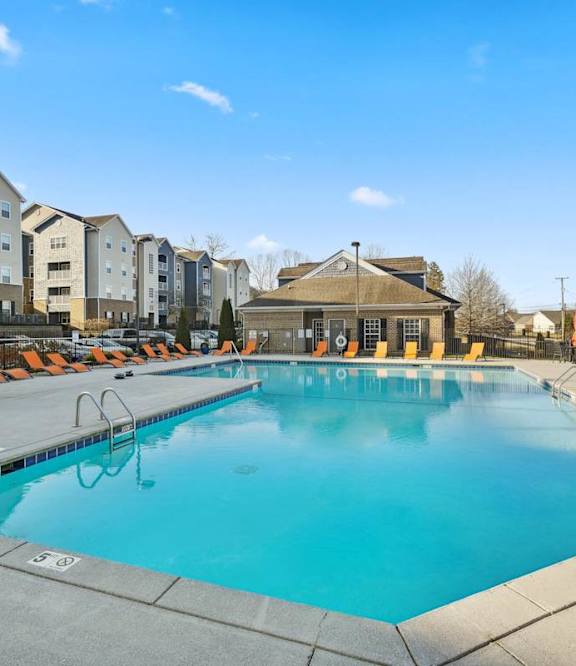 A large outdoor swimming pool surrounded by lounge chairs and buildings.