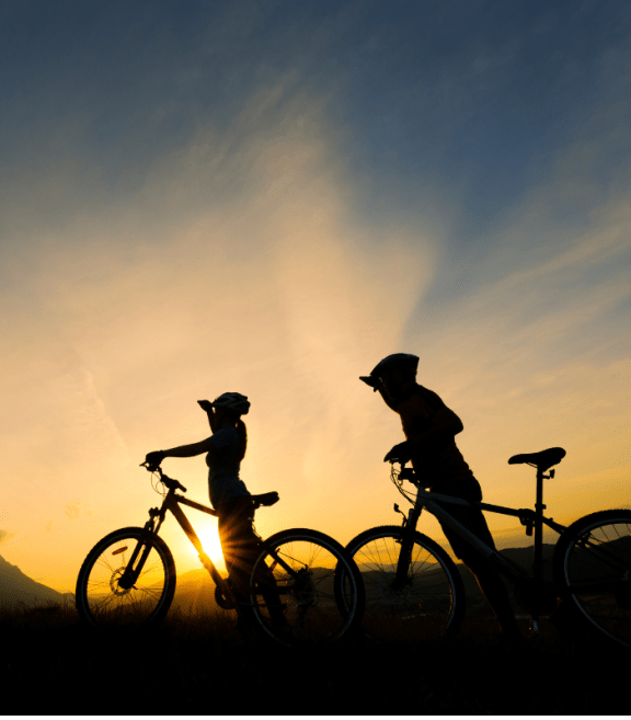 two people standing with bikes in front of the sunset