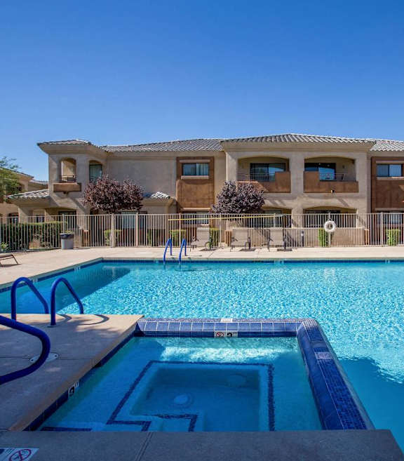 A large swimming pool in front of a building with a clear blue sky at Sereno Townhomes, Glendale, AZ.