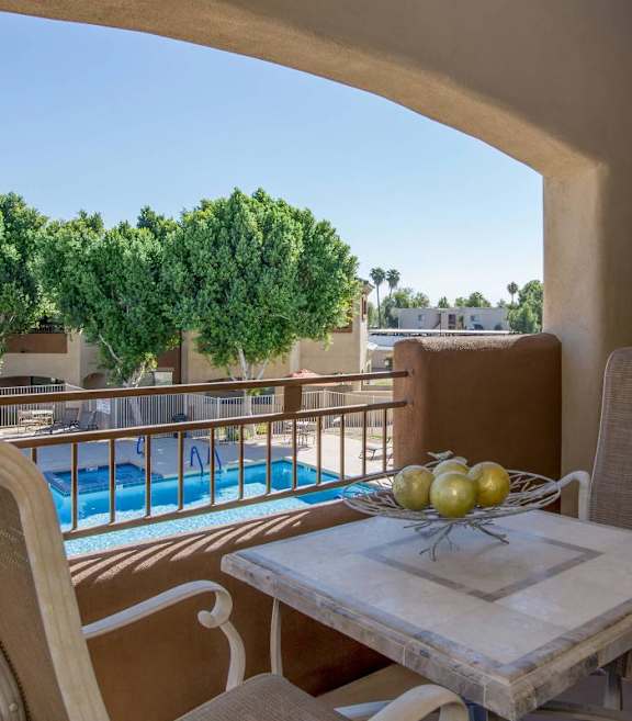 A table with a bowl of fruit on it sits on a balcony overlooking a pool at Sereno Townhomes, Glendale, AZ, 85302.