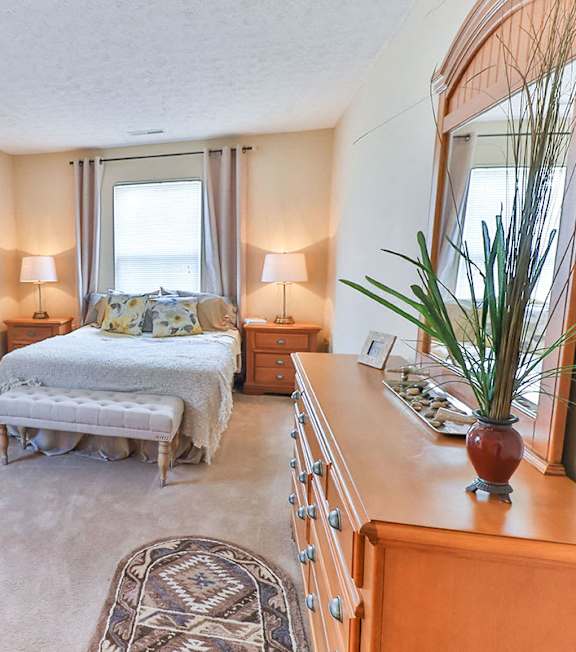 A bedroom with a bed, a chair, a dresser, and a mirror.