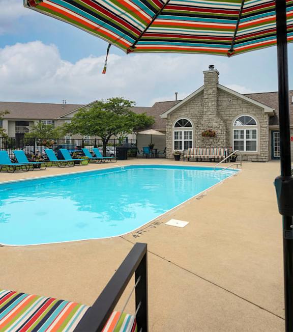 A pool with a striped umbrella and chairs.