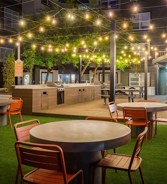A patio with a table and chairs is illuminated by string lights.