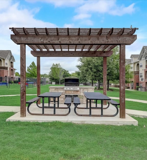 a picnic area with two picnic tables and a fire pit in the middle of a grassy