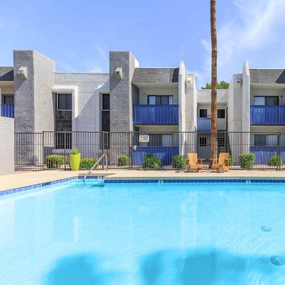 A swimming pool in front of a modern building with a blue fence around it.