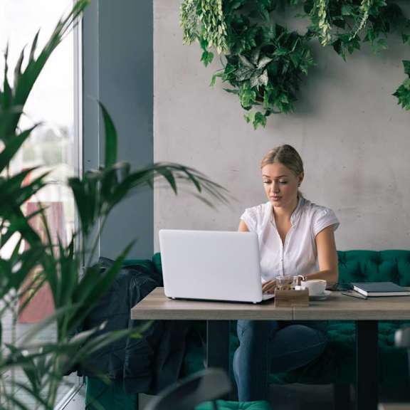 A woman is working on her laptop in a green-accented cafe.