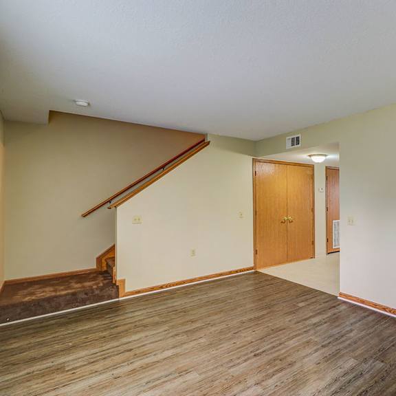 A room with a wooden floor and a staircase leading to the upper floor.