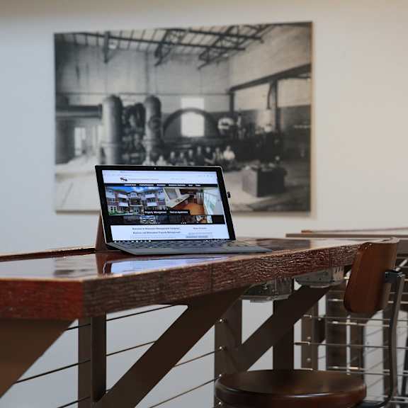 A laptop is open and displaying a video on a table in a room with a black and white photograph hanging on the wall.