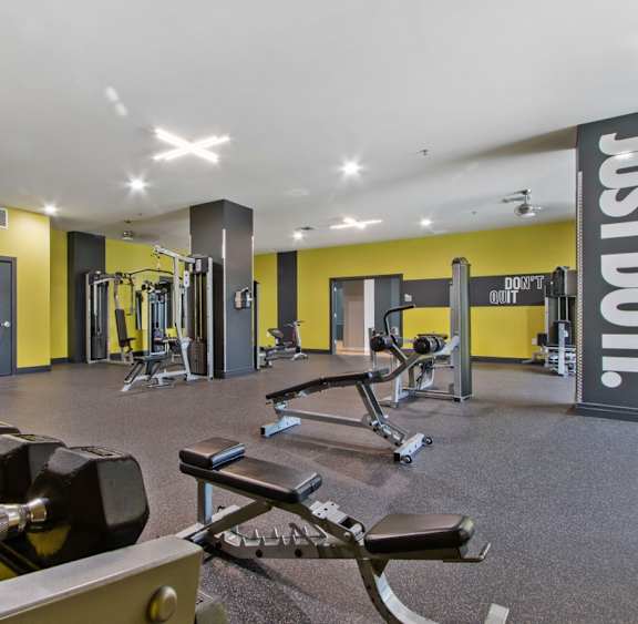 A gym with a variety of equipment including dumbbells, weight machines, and benches.