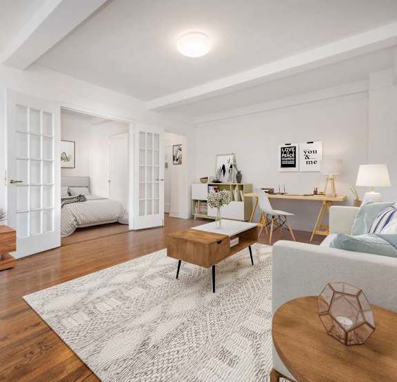 A living room with a white couch, a wooden coffee table, and a flat-screen TV mounted on the wall.at London Terrace Gardens, New York, 10011