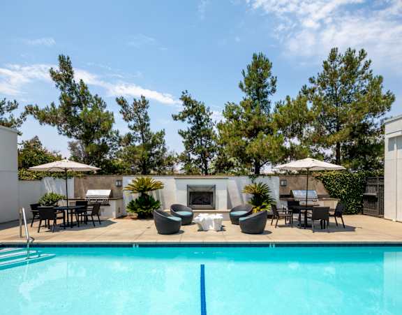 A swimming pool in a backyard with a patio and chairs.