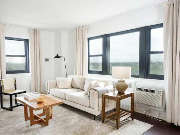 A living room with a white couch, a wooden coffee table, and a large window with a view of the ocean.