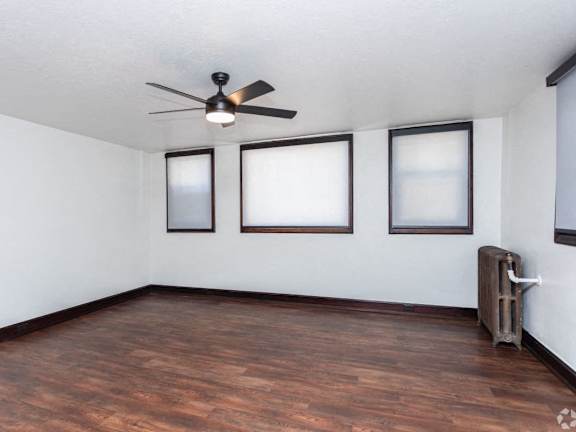 an empty living room with a ceiling fan and three windows