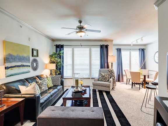 A modern living room with a grey sofa, a glass coffee table, and a ceiling fan.