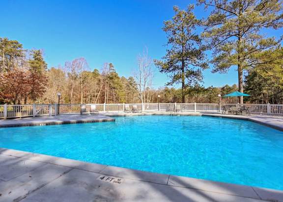 Swimming pool with lounge chairs and a table with an umbrella at our apartments in Peachtree Corners.