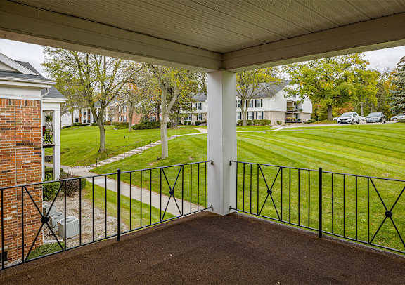 A view from a covered porch looking out at a grassy lawn and a row of houses.