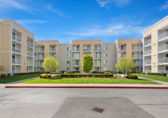 an exterior view of an apartment building with a lawn and trees in front of it