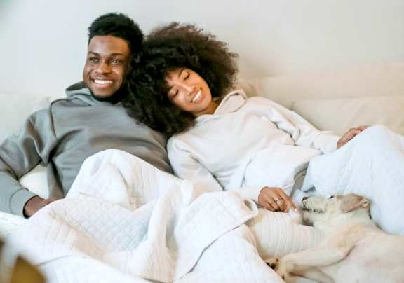 A man and woman are lying in bed with a dog.