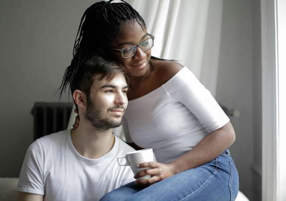 A man and a woman are sitting closely together, with the woman holding a cup.