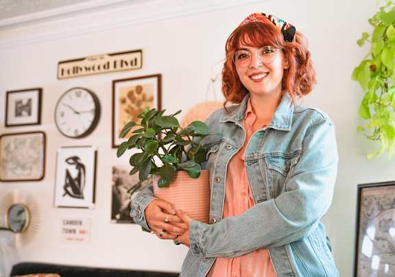 A woman with red hair is holding a plant and wearing a denim jacket.