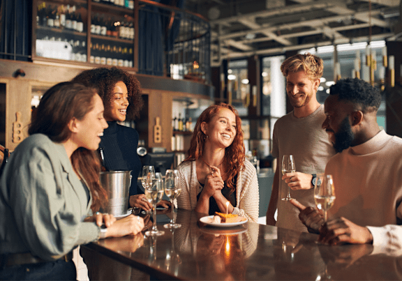 A group of people are gathered around a bar counter, enjoying drinks and conversation.