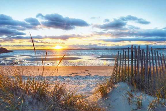 A beach scene with the sun setting behind the clouds.