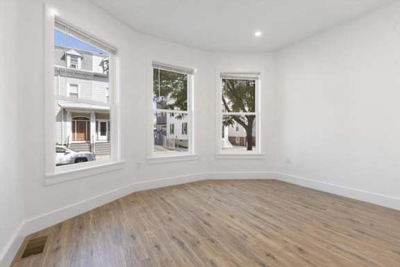 A room with white walls and wooden flooring, with two windows showing the outside view.