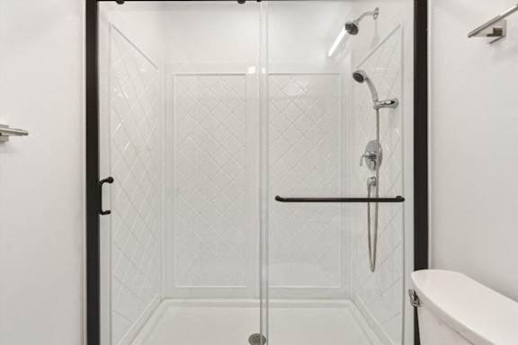 A white tiled shower with a glass door and a black handle.