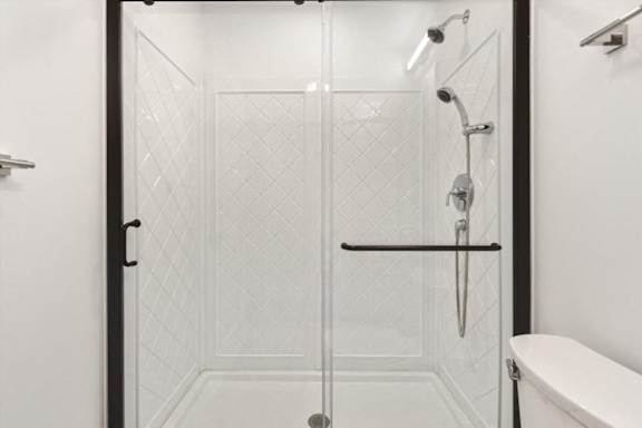 A white tiled shower with a glass door and a black handle.