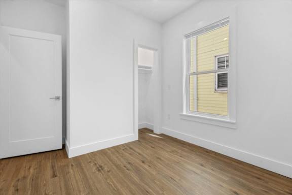 A room with a white door, a window with yellow blinds, and a wooden floor.