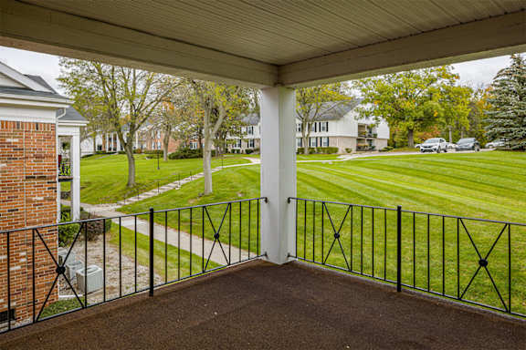 A view from a covered porch looking out at a grassy lawn and a row of houses at Glens of Bloomfield Apartments, Bloomfield Hills, MI