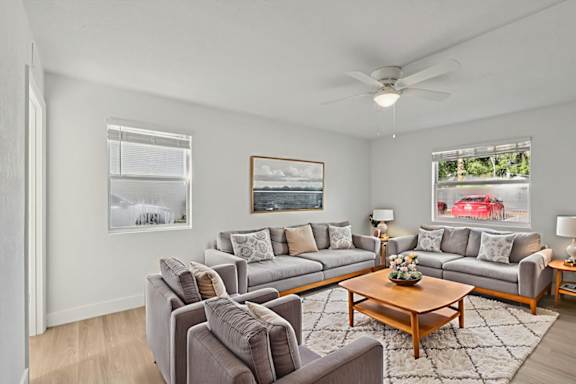 A living room with grey couches and a painting on the wall.