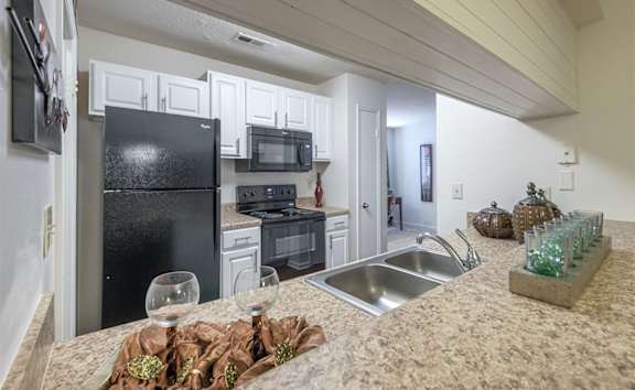 A kitchen with a black refrigerator, white cabinets, and a granite countertop.