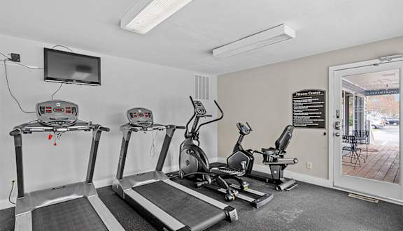 A gym with treadmills, elliptical machines, and a flat screen TV.