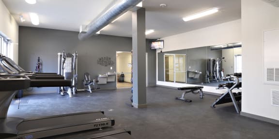 a gym with treadmills and other exercise equipment in a building with white walls at The Liberty Lofts, Gainesville