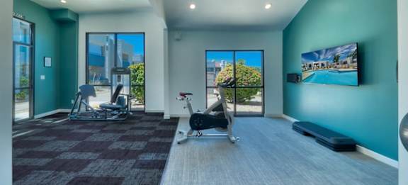 A room with a treadmill, exercise bike, and a television.