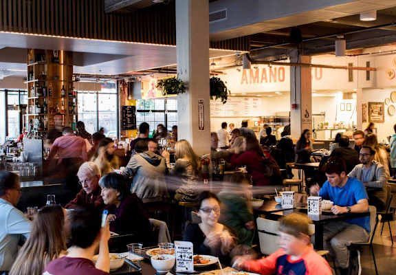 A busy restaurant with people sitting at the bar and others standing in the background.