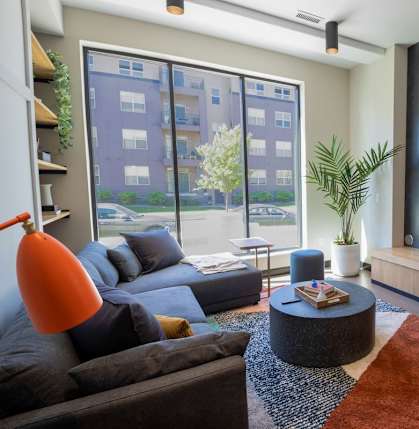 A living room with a grey couch, a coffee table, a television, and a large window.