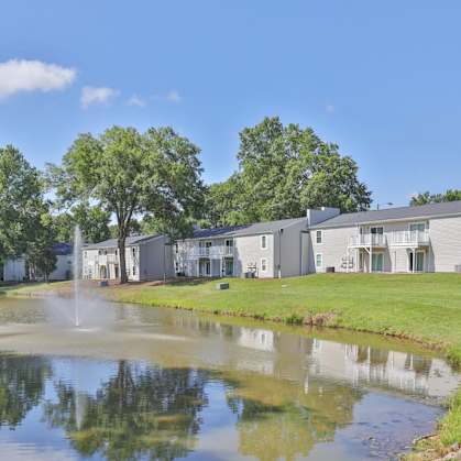 a pond with a fountain in front of a row of condominiums