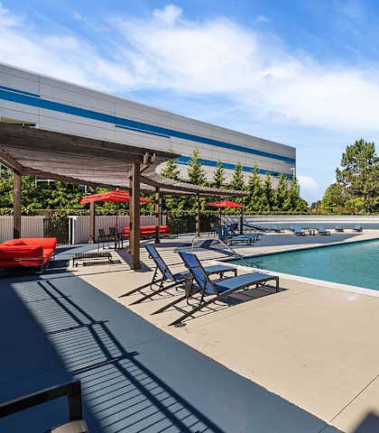 a swimming pool with chairs and umbrellas next to a building at Troy Place Apartments - Troy, MI, Michigan