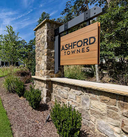 a sign for ashford towers on a stone wall next to a lawn and trees